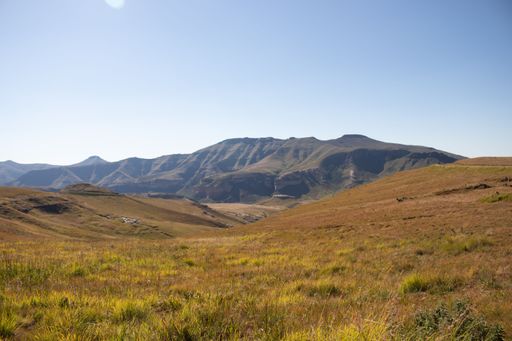 A landscape with large brown and green valleys with rocky mountains in the background