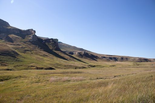 A large brown and green valley surrounded by rocky mountains against blue clear sky