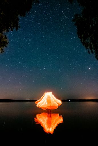 A vertical long exposure shot of light trails being reflected on the lake under a starry sky