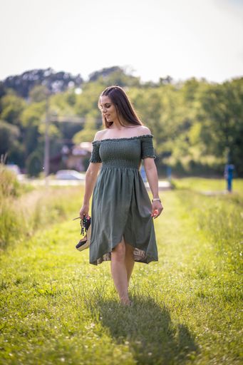 A beautiful shot of a Caucasian girl wearing a green dress standing on the grass field on a sunny day with blurred background