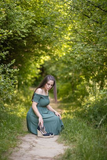A beautiful shot of a Caucasian girl wearing a green dress sitting on the grass field on a sunny day with blurred background