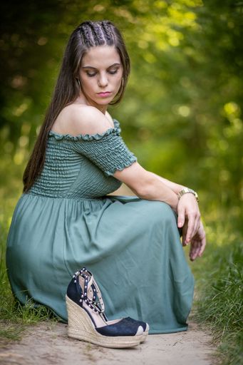 A beautiful shot of a Caucasian girl wearing a green dress sitting on a rock in a garden in daylight with blurred background