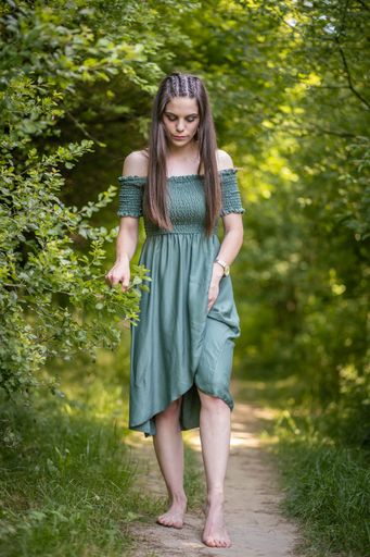 A beautiful shot of a Caucasian girl wearing a green dress standing on the grass field in the middle of green trees