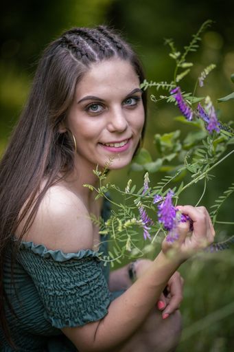 A closeup shot of a Caucasian girl with green brunch wearing a green dress on a sunny day with blurred background