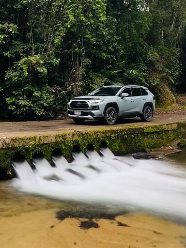 A vertical shot of a white modern SUV car parked on a low-water crossing in the rainforest near Millaa Millaa
