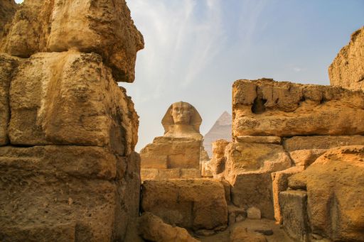 A shot of the Great Sphinx between the ruins and the Cheops Pyramid in the background located in Giza, Egypt.