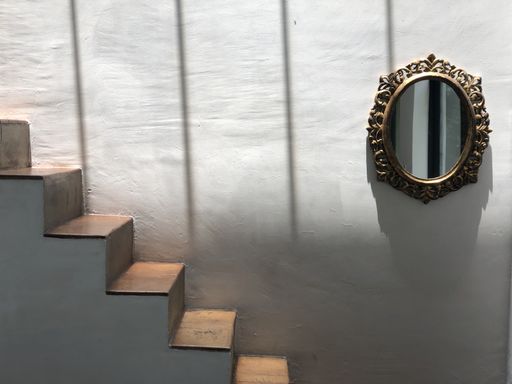 A light scenery of a minimalistic indoor wall near a narrow staircase with a vintage mirror