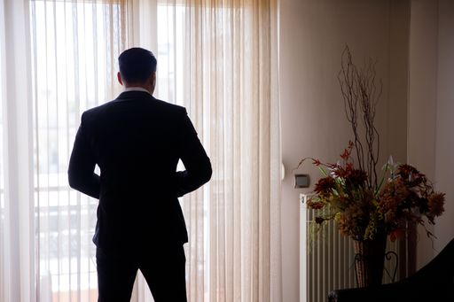 A handsome young man standing in front of the window captured from the back