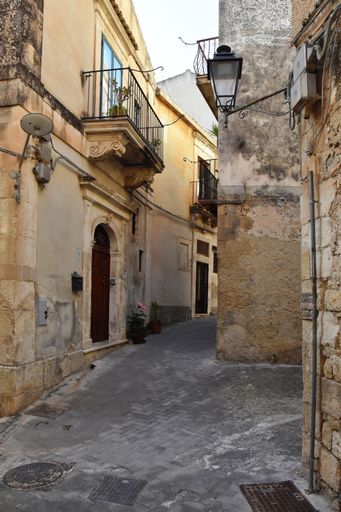 A vertical shot of a narrow alley between old buildings in the old town of Modica