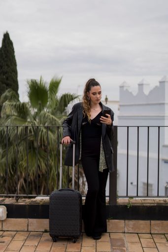 A young Caucasian female with a suitcase using her smartphone