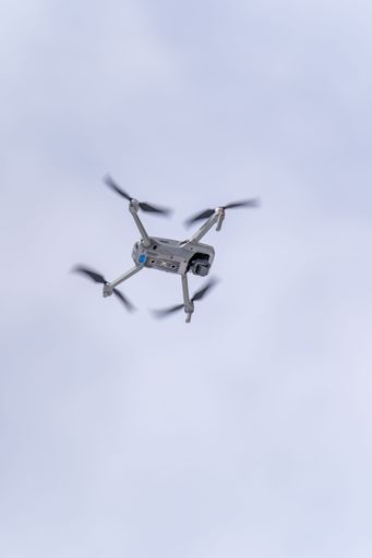 A vertical shot of a flying DJI drone through the air under cloudy sky