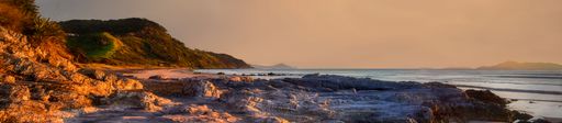 Sunrise at Mangawhai Heads beach, early morning sun highlighting foreground rocks and coastal cliffs