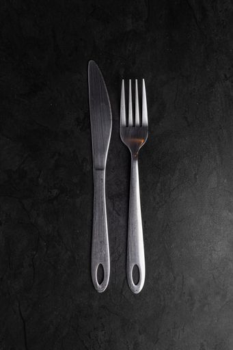 A vertical shot of old stainless steel knife and fork on a black surface