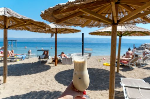 A female holding glass of cold iced coffee on the beach