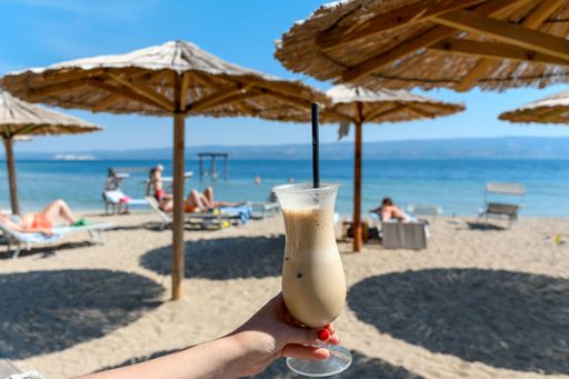 A female holding glass of cold iced coffee on the beach