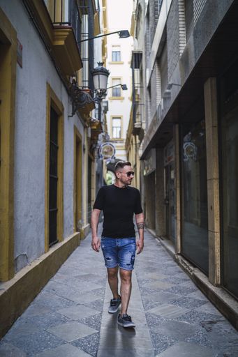 A young Caucasian male wearing a black shirt and shorts walking near tall buildings