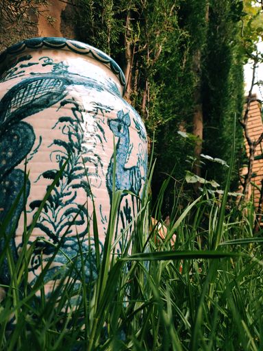 Jarrón antiguo con diseños azules en un jardín verde.