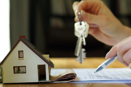 A female hand holding keys next to a miniature house - real estate business concept