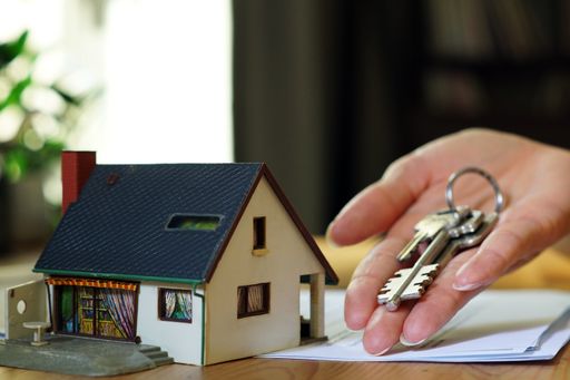 A female hand holding keys next to a miniature house - real estate business concept