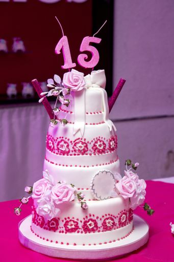 A vertical closeup shot of a three-layered 15th birthday cake with pink rose decorations