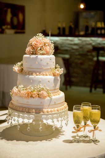 A vertical closeup shot of a beautiful three-layered cake with rose decorations and glasses of champagne on the table