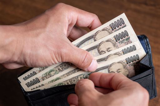 A closeup of a person's hands counting the Japanese banknotes inside his black leather wallet