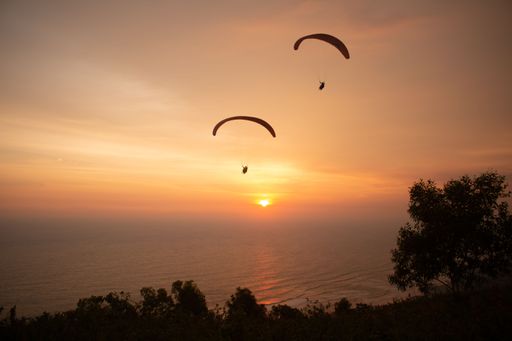 Paragliding over the ocean and treetops while golden sunset at Parangtritis beach on Java island in Indonesia