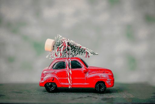 A miniature red toy car with a Christmas tree on the top on a gray background