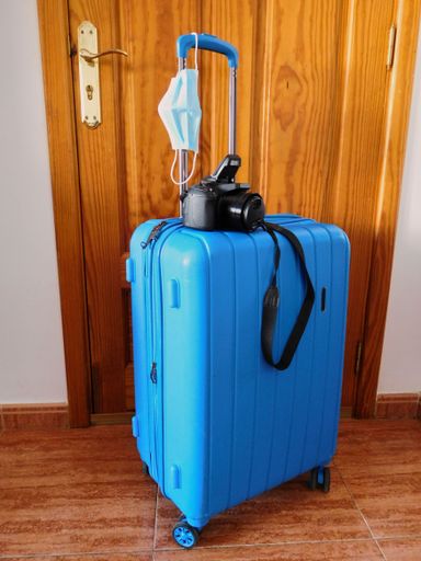 The travel suitcase with a camera and medical mask. The concept of traveling during coronavirus, vertical