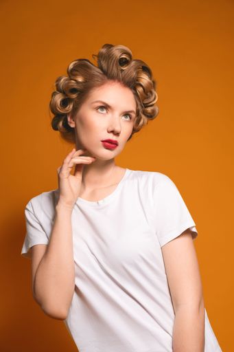 A vertical portrait of an attractive female with curlers on her hair on yellow background