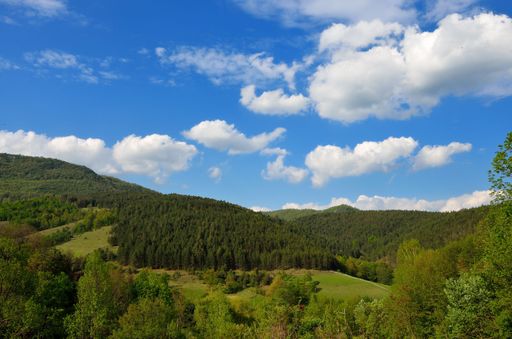 A mesmerizing view of a green mountains over green fields under blue cloudy sky