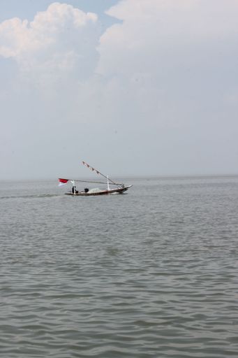 A vertical shot of a boat on the sea with a cloudy sky background
