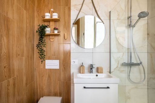 A fancy bathroom with ceramic wall, circular mirror, shower head and white sink