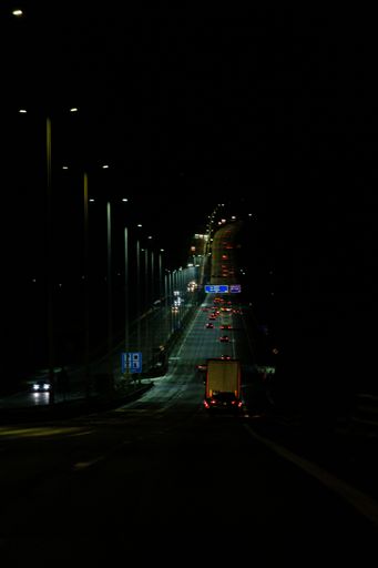 A vertical shot of the road with cars illuminated by street lamps.
