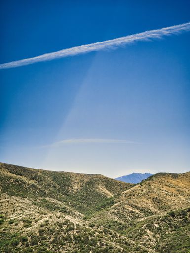 A vertical shot of a steppe landscape and a track of a plane in the sky