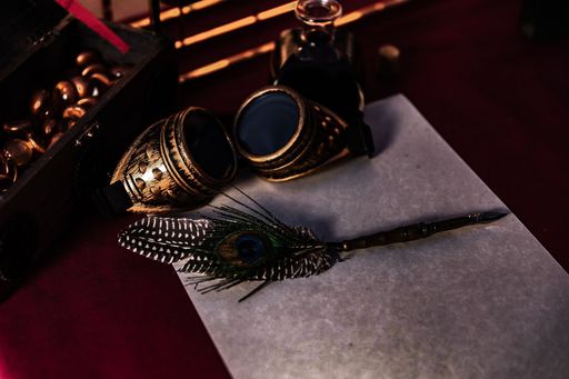 A high angle shot of a beautiful feather pen on a blank paper next to vintage steampunk glasses
