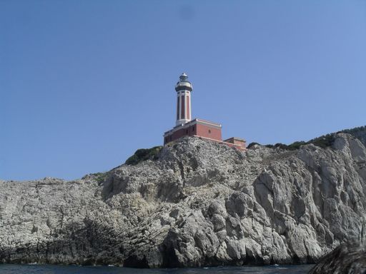 A beautiful view of a lighthouse on the rocky cliff by the sea under a blue sunny sky
