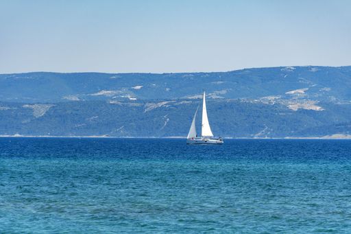 A single boat sailing in a sea with mountains on the background