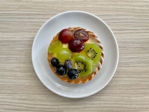 Top view of a delicious tart with fresh grapes, kiwi and blueberry on white plate on wooden table
