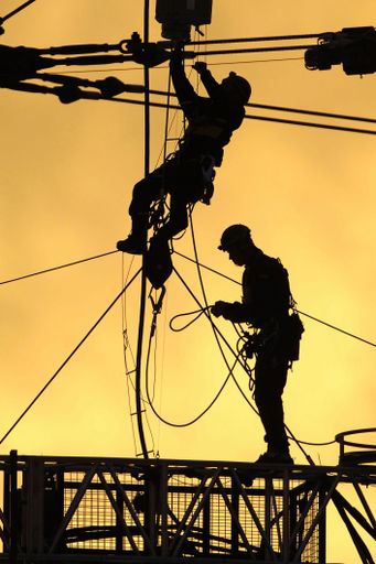 A vertical shot of workers on a crane at sunset