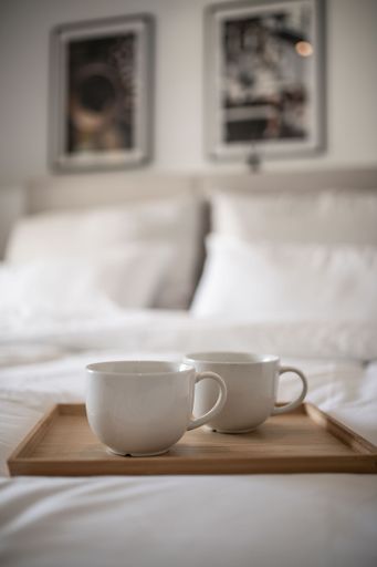 A cozy bed with clean white sheets and coffee mugs on a wooden tray