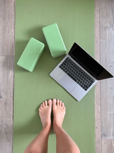 A vertical top view of a person on a yoga matt with equipment and a laptop for an online yoga class