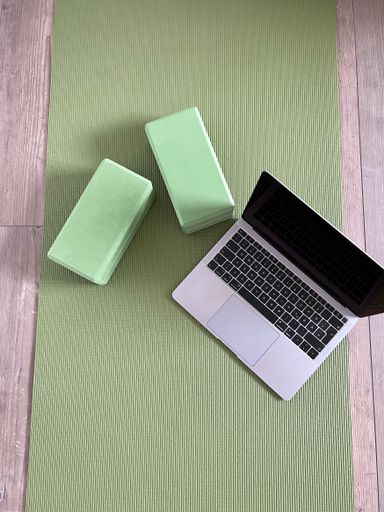 A vertical top view of a green yoga matt with yoga equipment and a laptop for an online class