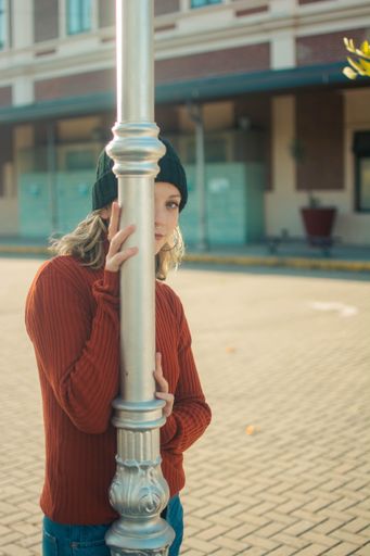 A vertical shot of a cute Hispanic girl in a black hat peeking from behind a street pole