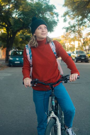 A vertical shot of a cute Hispanic girl in a black hat riding a bicycle