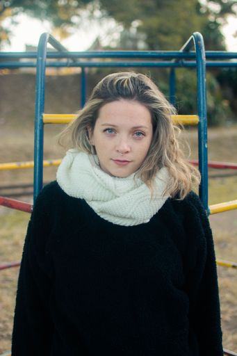 Vertical shot of young girl with piercings in black sweater and white scarf posing in front of camera on sunny day in garden