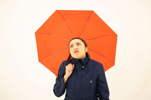 A young bored Hispanic female in a blue coat waiting for rain, holding an umbrella on a white background