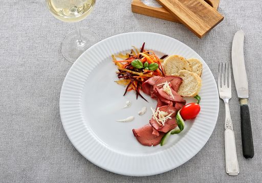 A high angle shot of meat with salad and bread in a white plate on the table