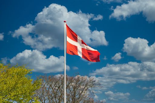 The waving flag of Denmark on a pipe in a field under the sunlight and a blue sky
