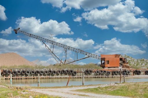 An old weathered construction crane by the lake under a cloudy sky at daytime